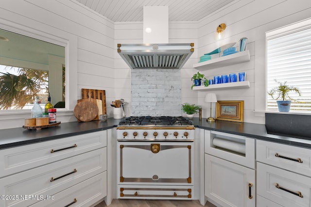 kitchen featuring range, wood walls, island range hood, and white cabinetry