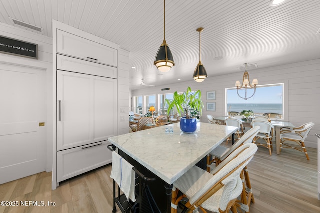 kitchen with white cabinets, light stone counters, light hardwood / wood-style floors, hanging light fixtures, and a kitchen island