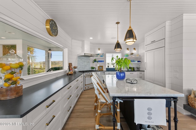 kitchen featuring light wood-type flooring, wall chimney exhaust hood, gas stove, and white cabinetry