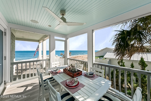 sunroom with ceiling fan, a beach view, and a water view