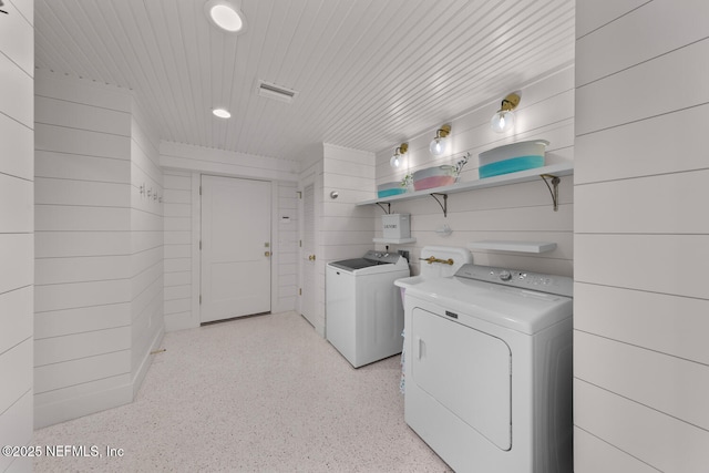 clothes washing area with separate washer and dryer and wooden walls