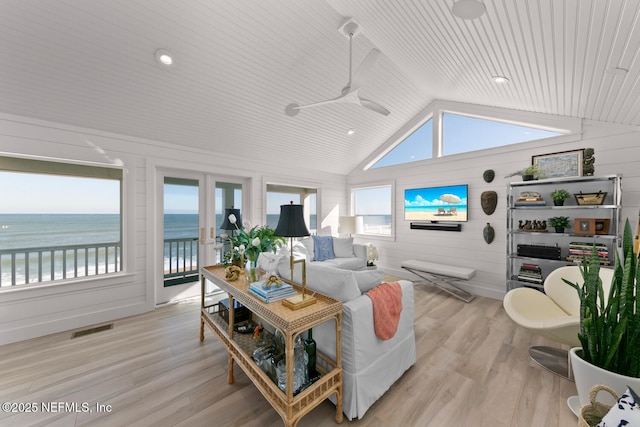 living room with vaulted ceiling, light hardwood / wood-style flooring, wooden walls, ceiling fan, and a water view