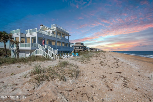 back house at dusk with a beach view and a water view