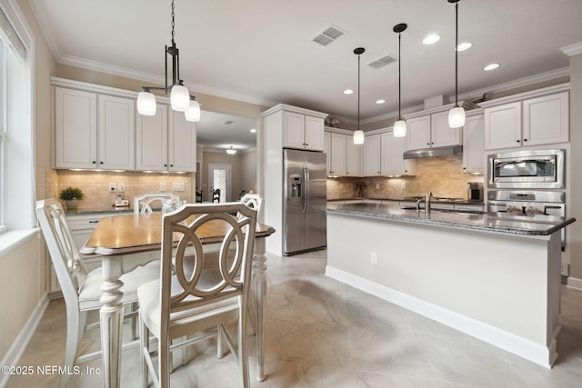 kitchen with decorative backsplash, stainless steel appliances, hanging light fixtures, and a center island with sink