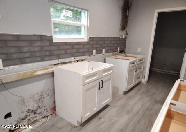 kitchen featuring white cabinets, decorative backsplash, light wood-type flooring, and sink