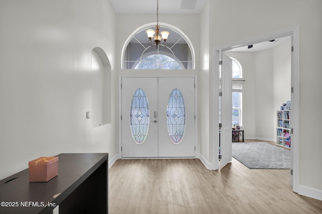 entryway featuring french doors, a towering ceiling, a healthy amount of sunlight, and an inviting chandelier