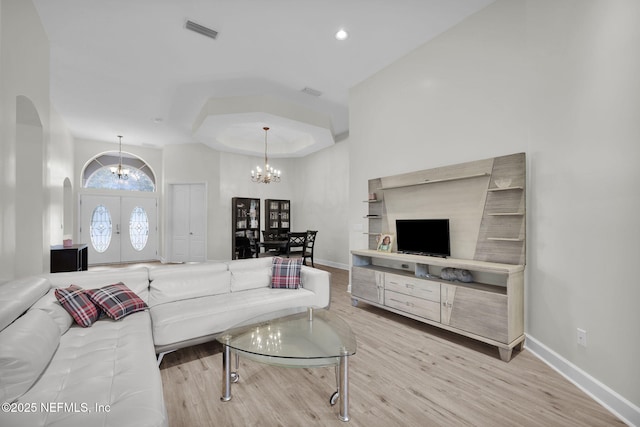 living room with french doors, light hardwood / wood-style flooring, an inviting chandelier, and a raised ceiling