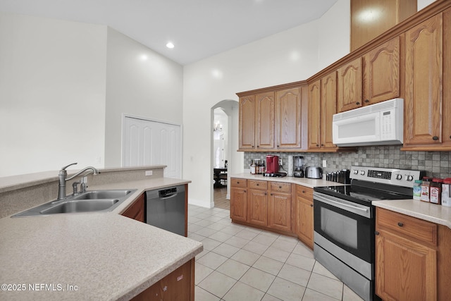 kitchen featuring sink, light tile patterned floors, a towering ceiling, tasteful backsplash, and stainless steel appliances