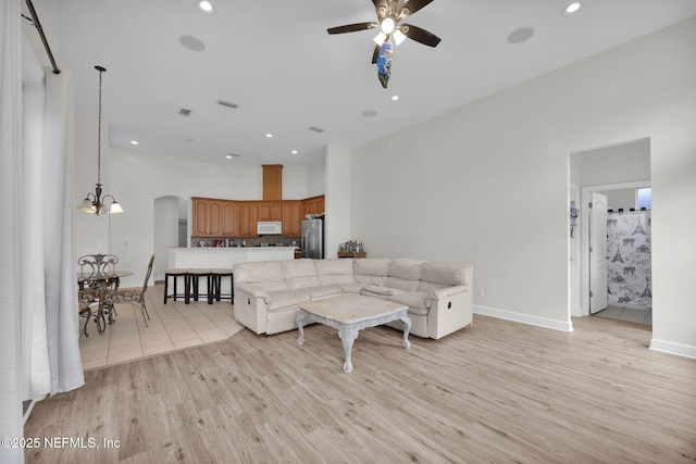 living room featuring ceiling fan with notable chandelier and light wood-type flooring