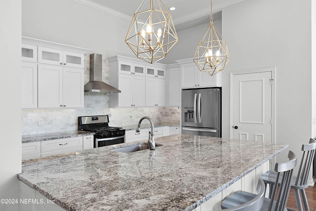 kitchen with sink, wall chimney exhaust hood, pendant lighting, white cabinets, and appliances with stainless steel finishes