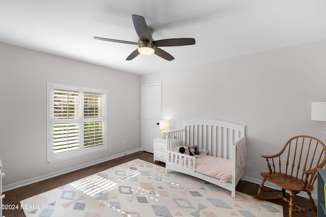 bedroom featuring hardwood / wood-style floors, ceiling fan, and a nursery area