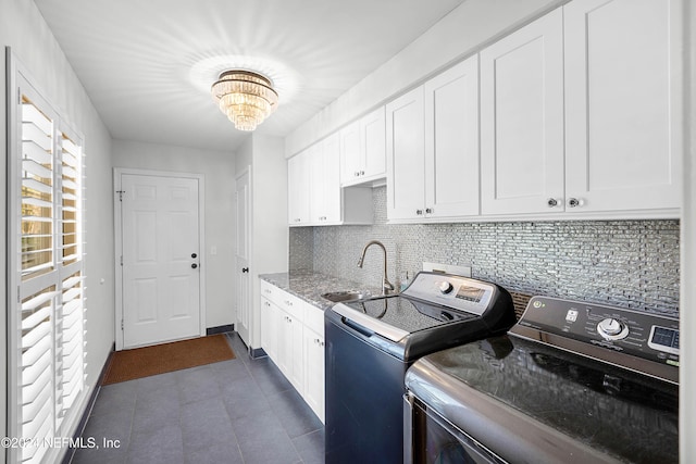 clothes washing area with cabinets, an inviting chandelier, dark tile patterned flooring, sink, and washing machine and clothes dryer