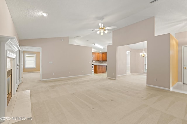 unfurnished living room featuring a textured ceiling, vaulted ceiling, a tiled fireplace, light carpet, and ceiling fan with notable chandelier