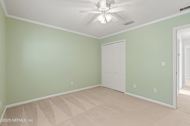 unfurnished bedroom featuring ceiling fan, a textured ceiling, light carpet, a closet, and ornamental molding