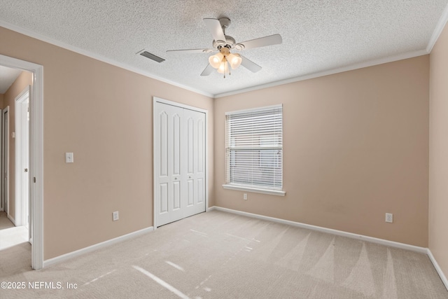 unfurnished bedroom with ceiling fan, a closet, light colored carpet, and crown molding