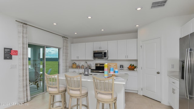 kitchen featuring a breakfast bar, stainless steel appliances, a kitchen island with sink, light tile patterned floors, and white cabinetry