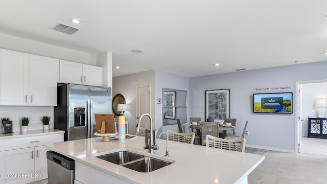 kitchen with white cabinetry, sink, stainless steel appliances, a kitchen island with sink, and light tile patterned flooring