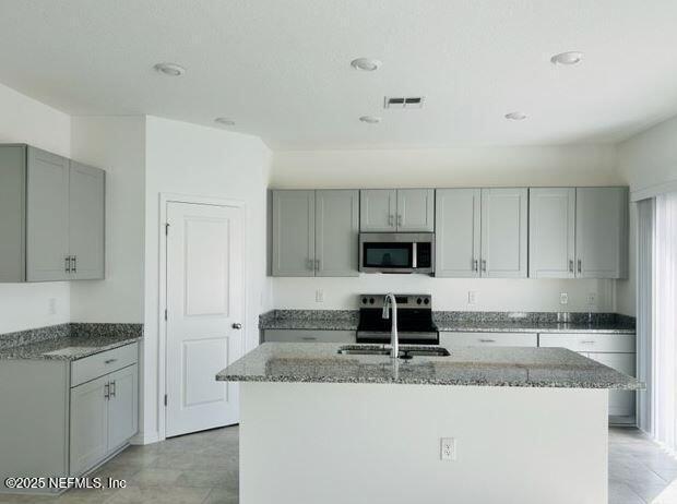 kitchen featuring stainless steel appliances, gray cabinets, a center island with sink, and sink