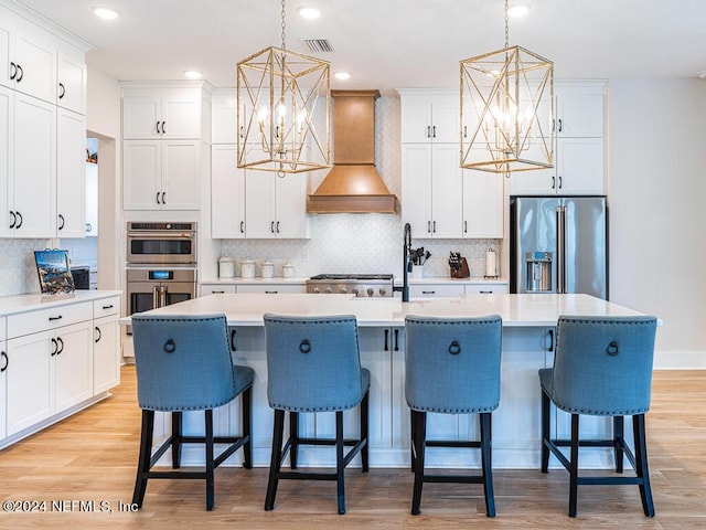 kitchen featuring decorative light fixtures, custom range hood, stainless steel appliances, and a kitchen island with sink