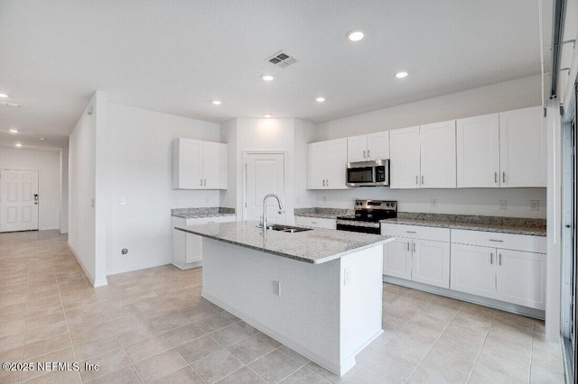 kitchen with appliances with stainless steel finishes, an island with sink, sink, white cabinets, and light stone countertops