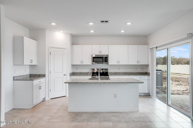 kitchen featuring white cabinetry, appliances with stainless steel finishes, light stone countertops, and an island with sink