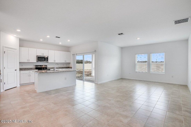 kitchen with light tile patterned floors, stone counters, white cabinetry, appliances with stainless steel finishes, and an island with sink