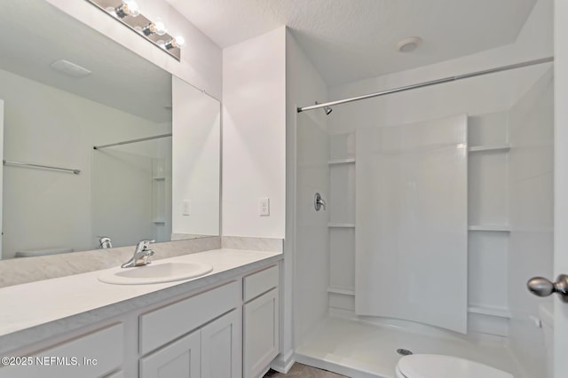 bathroom with a textured ceiling, vanity, toilet, and walk in shower