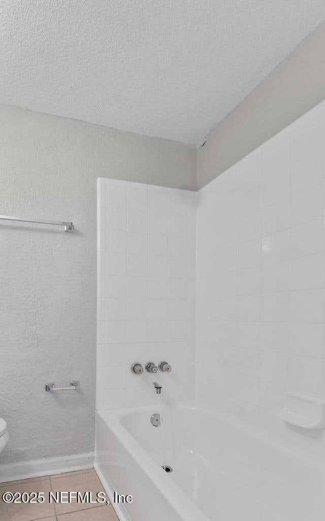 bathroom with tile patterned flooring, a textured ceiling, bathing tub / shower combination, and toilet