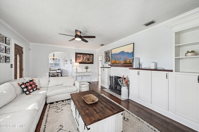 living room with built in shelves, dark hardwood / wood-style flooring, a textured ceiling, ceiling fan with notable chandelier, and ornamental molding