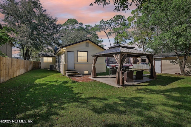 back house at dusk with a gazebo, a patio, central AC, and a lawn