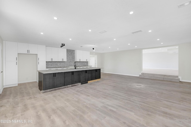 kitchen featuring backsplash, a large island with sink, white cabinets, sink, and light hardwood / wood-style floors