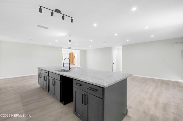 kitchen featuring gray cabinetry, sink, light stone counters, light hardwood / wood-style flooring, and an island with sink