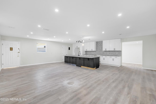 kitchen with white cabinets, sink, light hardwood / wood-style flooring, decorative backsplash, and an island with sink