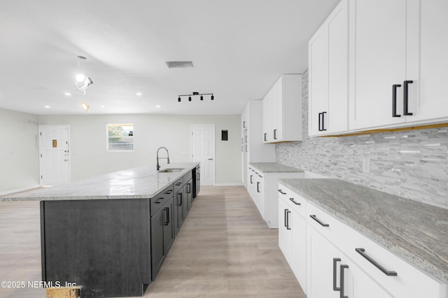 kitchen with tasteful backsplash, light stone counters, a kitchen island with sink, sink, and white cabinets