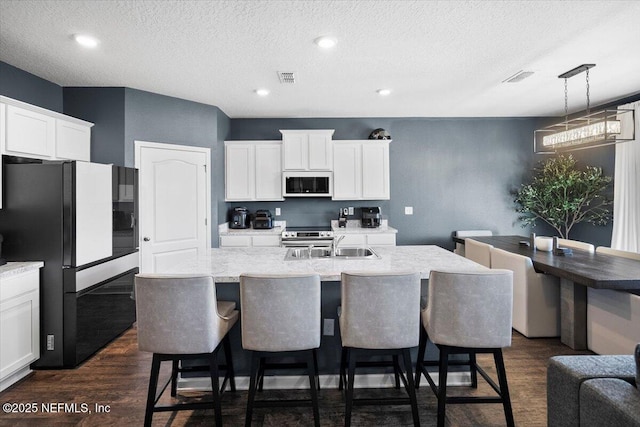 kitchen with a textured ceiling, black refrigerator, an island with sink, and decorative light fixtures