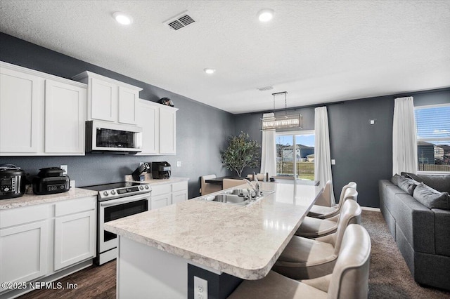 kitchen featuring pendant lighting, a kitchen island with sink, white cabinets, electric stove, and sink