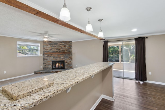 kitchen with ornamental molding, ceiling fan, pendant lighting, dark hardwood / wood-style floors, and a stone fireplace