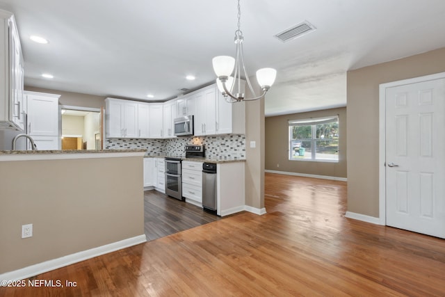 kitchen with white cabinets, dark wood-type flooring, decorative light fixtures, and appliances with stainless steel finishes