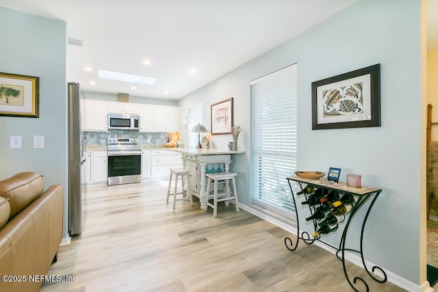 kitchen with a skylight, white cabinetry, light hardwood / wood-style flooring, backsplash, and appliances with stainless steel finishes