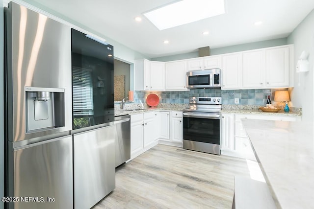 kitchen with light hardwood / wood-style flooring, a skylight, appliances with stainless steel finishes, tasteful backsplash, and white cabinetry