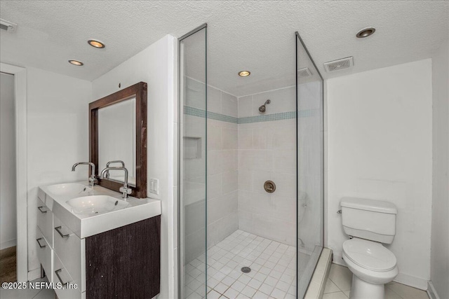 bathroom featuring vanity, tile patterned floors, toilet, a textured ceiling, and a tile shower