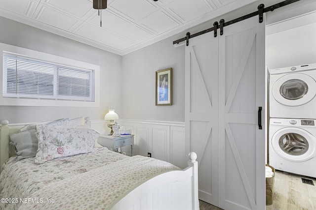 bedroom with ceiling fan, stacked washer / dryer, hardwood / wood-style flooring, and a barn door