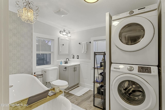 clothes washing area with stacked washing maching and dryer, light wood-type flooring, a notable chandelier, and sink