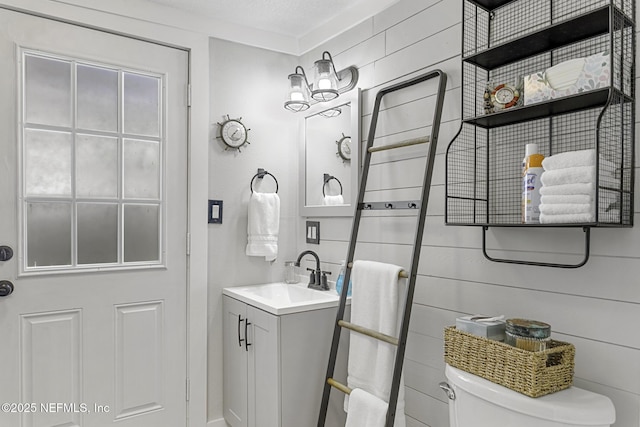 bathroom featuring toilet, a textured ceiling, wood walls, and vanity