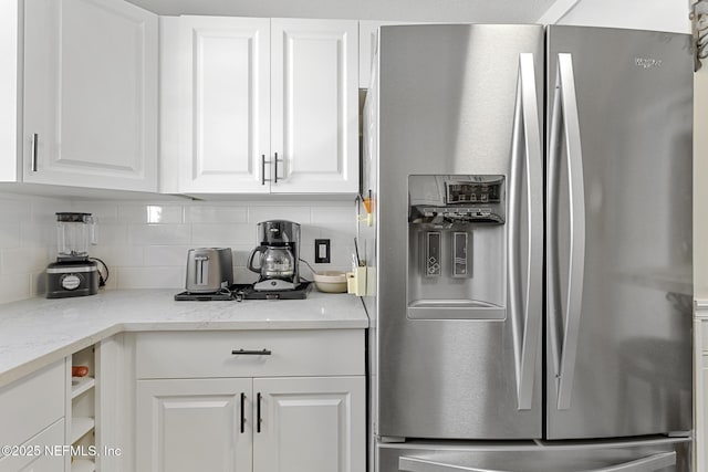 kitchen with stainless steel fridge with ice dispenser, decorative backsplash, white cabinets, and light stone countertops