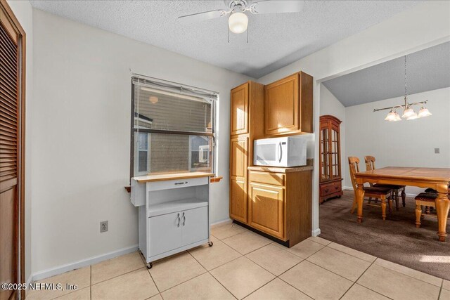 kitchen featuring a textured ceiling, light tile patterned floors, ceiling fan with notable chandelier, and decorative light fixtures