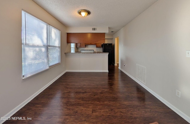 kitchen with kitchen peninsula, a textured ceiling, dark hardwood / wood-style floors, and black fridge