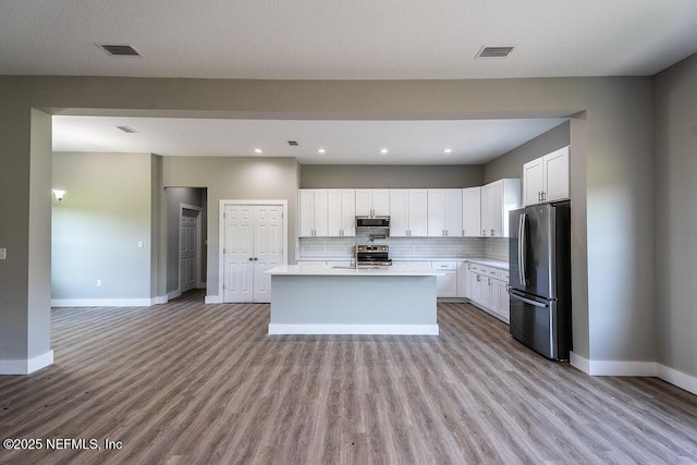 kitchen featuring tasteful backsplash, appliances with stainless steel finishes, an island with sink, white cabinets, and light wood-type flooring