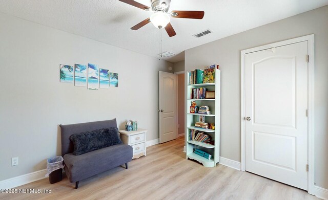 living area with ceiling fan, light hardwood / wood-style floors, and a textured ceiling