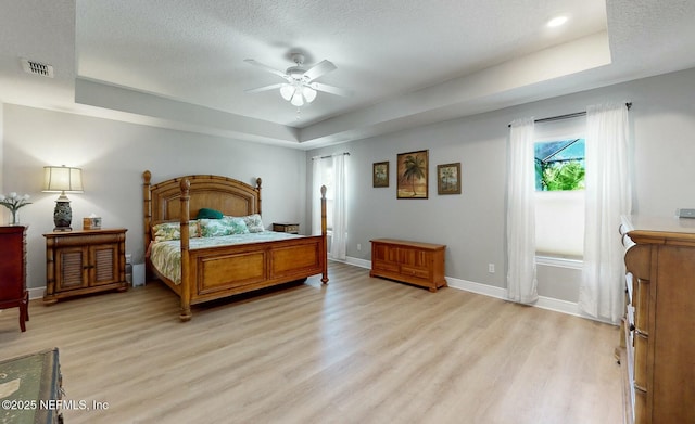 bedroom with a tray ceiling, ceiling fan, a textured ceiling, and light wood-type flooring